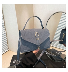 Detail of blue denim handbag featuring gold horsebit buckle and adjustable shoulder strap
