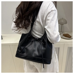 Detailed view of black tote bag with slender bow decoration worn on the shoulder