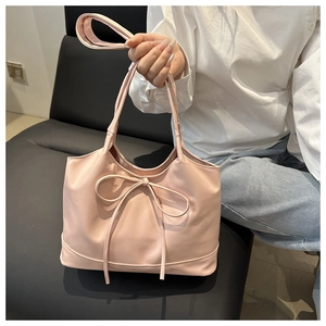Close-up of light pink tote bag with bow detail held by a model in a white shirt
