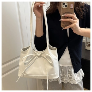 Détail d'un sac à bandoulière blanc minimaliste avec un nœud décoratif et une fine lanière