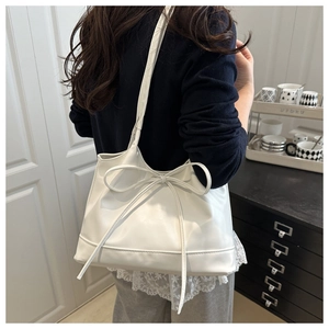 Close-up of white leather tote bag with bow detail on a shoulder model outdoors