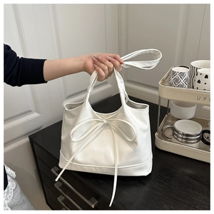 Close-up of white minimalist square bag with decorative bow detail and PU leather texture