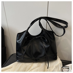 Detail of black faux leather handbag featuring a delicate ribbon bow and pleated texture