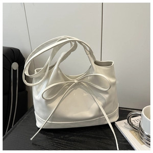 Detailed view of white glossy handbag featuring a large ribbon bow and double handles