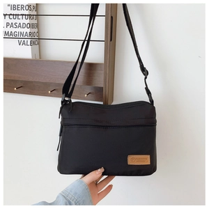 Detail of minimalist black nylon crossbody bag with zipper pocket and leather logo patch