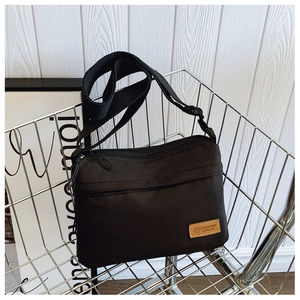 Close-up of black nylon crossbody bag with multi-zippered compartments and leather logo