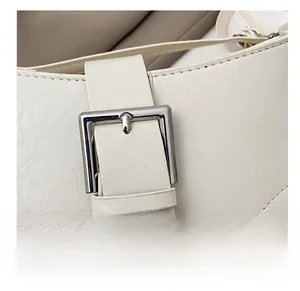 Close-up of white leather shoulder bag featuring a silver metal buckle and strap details