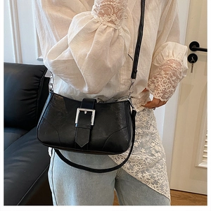 Detailed view of black leather shoulder bag featuring a large silver square metal buckle