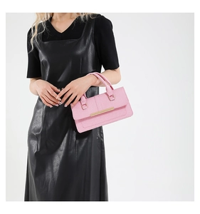 Détail d'un sac à main rose en cuir texturé avec une élégante barre métallique dorée