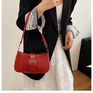 Detail of red leather underarm bag featuring silver buckle and elegant curved stitching