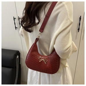 Detail of burgundy woven hobo bag with gold bow clasp worn by model for size reference