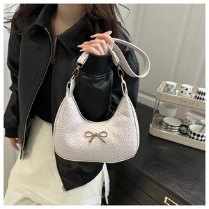 Close-up of white hobo bag with embossed texture and gold bow detail on a shoulder