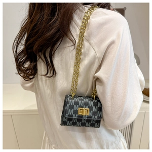 Detail of a mini chain crossbody bag with black jacquard M pattern on a white blouse model