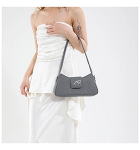 Close-up of grey baguette bag with silver metal bow detail and fine texture finish