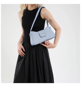 Close-up of light blue shoulder bag with silver metal bow buckle on white background