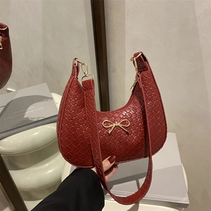 Sac demi-lune bordeaux avec texture tressée et nœud doré en décor de style de vie