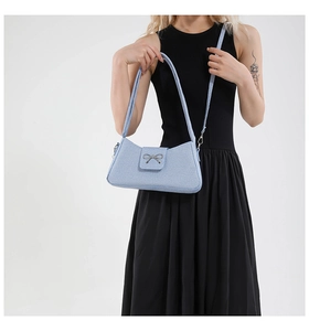 Detail of light blue textured bag featuring a metallic bow and elegant carry strap