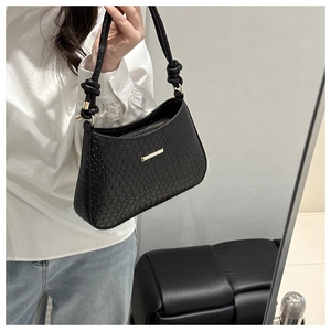 Détail d'un sac porté épaule tressé noir avec garnitures dorées et bandoulière à nœuds
