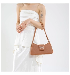 Close-up of caramel leather shoulder bag featuring a silver metal bow buckle detail