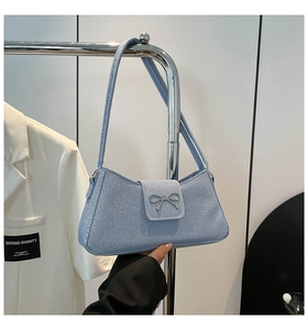 Close-up of light blue baguette bag with silver metal bow and textured fabric detail
