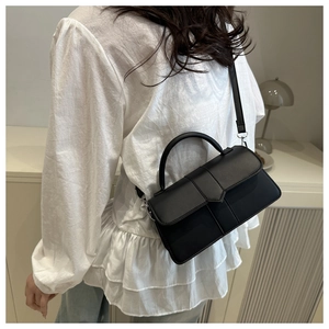 Model wearing a black rectangle handbag with flap design and adjustable strap in a room
