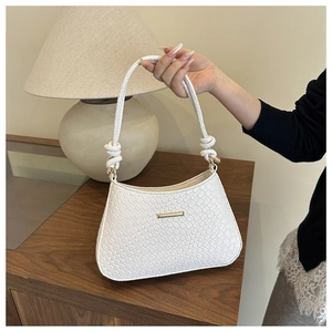 Detail of white woven texture shoulder bag with gold metal trim and knotted strap
