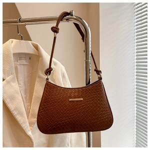 Close-up of brown woven underarm bag with gold metal detail and knotted shoulder strap