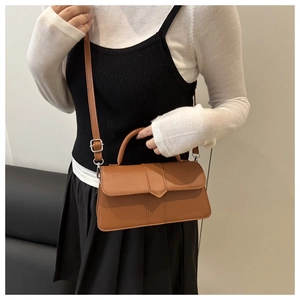 Brown PU leather crossbody bag with triangular flap detail worn by model on plain background
