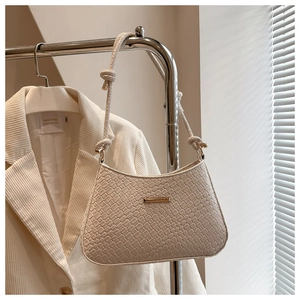 Detail of cream woven shoulder bag with golden hardware and knotted strap on stand