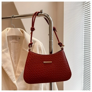 Detail of burgundy textured leather underarm bag with gold buckle and knotted strap