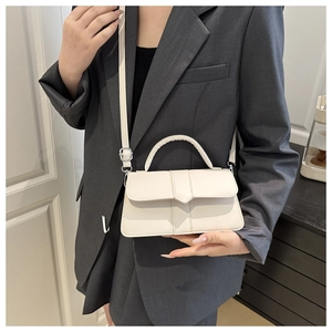 Detail of a beige PU leather rectangular crossbody bag with handle worn over a grey blazer