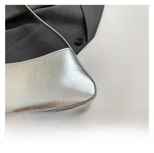 Detail of silver metallic shoulder bag with smooth texture on a minimalist background