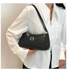 Close-up of a glossy black patent leather shoulder bag with a gold square buckle detail