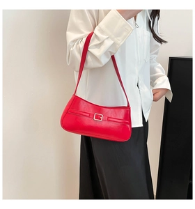 Model side view of a red leather shoulder bag with a metal buckle and matte finish