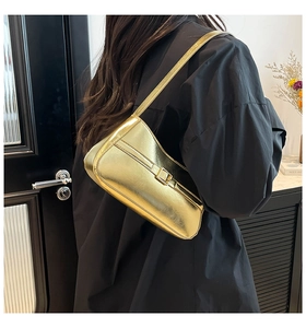 Close-up of metallic gold shoulder bag with square buckle worn by a model