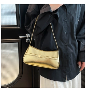 Close-up of metallic gold baguette bag with decorative buckle on a black shirt background