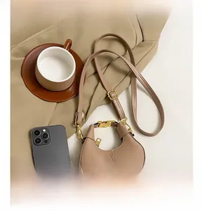 Mini crescent crossbody bag in beige leather shown next to a smartphone for size scale