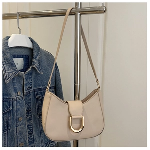 Close-up of beige crescent underarm bag featuring a prominent gold D-ring buckle detail