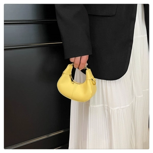 Close-up of lemon yellow mini crescent handbag held by a model in black and white outfit