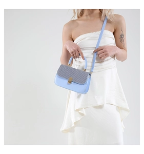 Detail of light blue crossbody bag with grey woven flap and gold buckle on a model