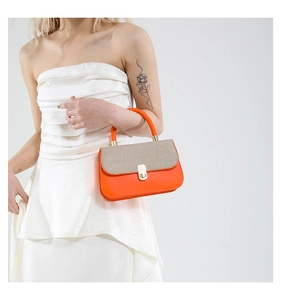 Close-up of bright orange handbag with beige woven flap and gold metal twist lock detail