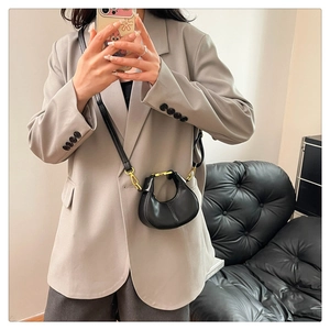 Detail of a mini black crescent bag with gold buckle on a grey blazer outfit