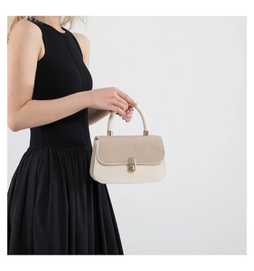 Detail of beige underarm bag with woven texture lid and golden metal clasp on model