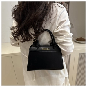 Detail of black faux leather tote with golden 'FASHION BAG' text and knotted handle accents