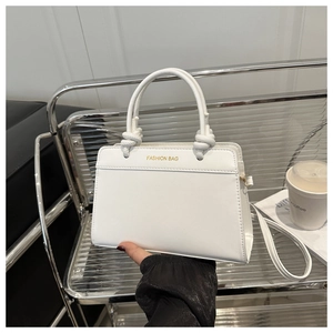 Detail of white minimalist handbag featuring knotted handle and gold FASHION BAG text