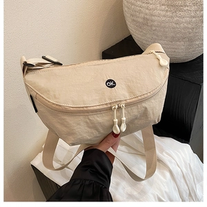 Détail du sac demi-lune en nylon beige avec logo OK et fermetures éclair à la main