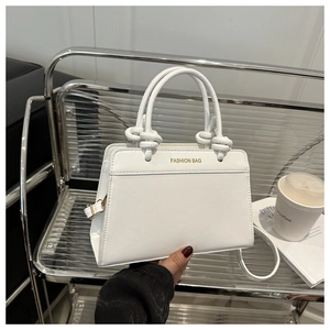 Detail of white PU tote bag with knot handles and gold hardware in modern setting