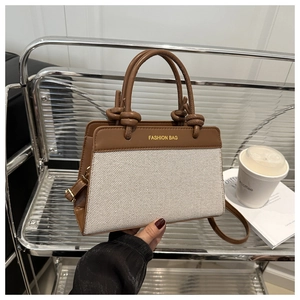 Detail of brown leather and beige canvas handbag with circular knot handle and gold text