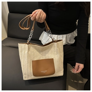 Detail of woven straw tote bag featuring brown leather pocket and metal chain strap