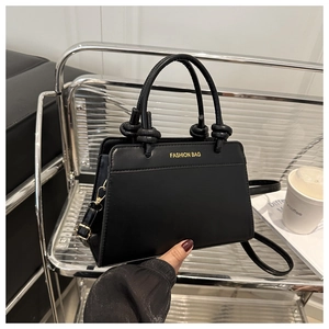 Close-up of matte black leather tote with gold logo and detachable shoulder strap